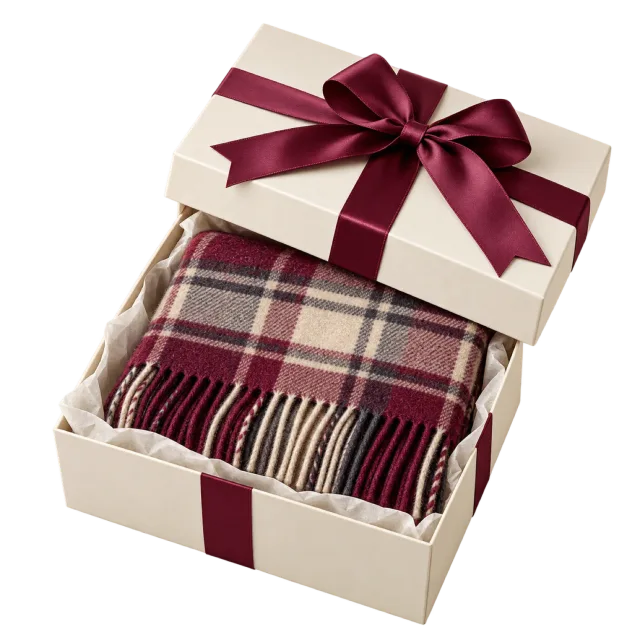 An open cream box containing a folded burgundy plaid scarf, with a matching ribbon bow on the lid