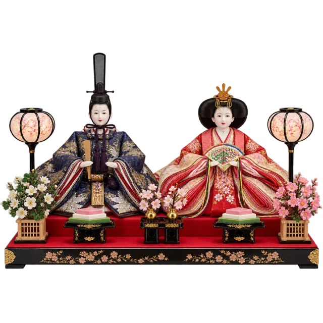 Two ornate seated dolls in layered clothing displayed on a red platform with lanterns and floral decorations