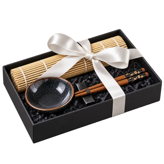 A black gift box containing a bamboo rolling mat, small dark dish and utensils, tied with a white bow