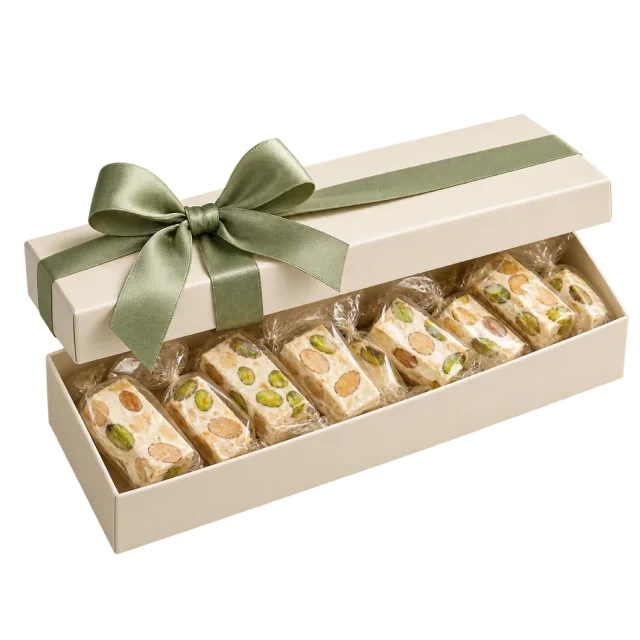 An open cream box of pale nut-studded nougat pieces with a sage-green ribbon
