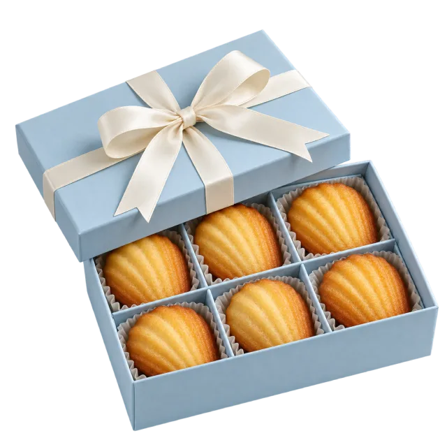A pale blue gift box containing golden shell-shaped madeleines with a cream bow on the lid