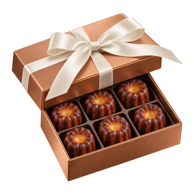 A brown gift box with dark fluted canele-shaped pastries and a cream ribbon bow