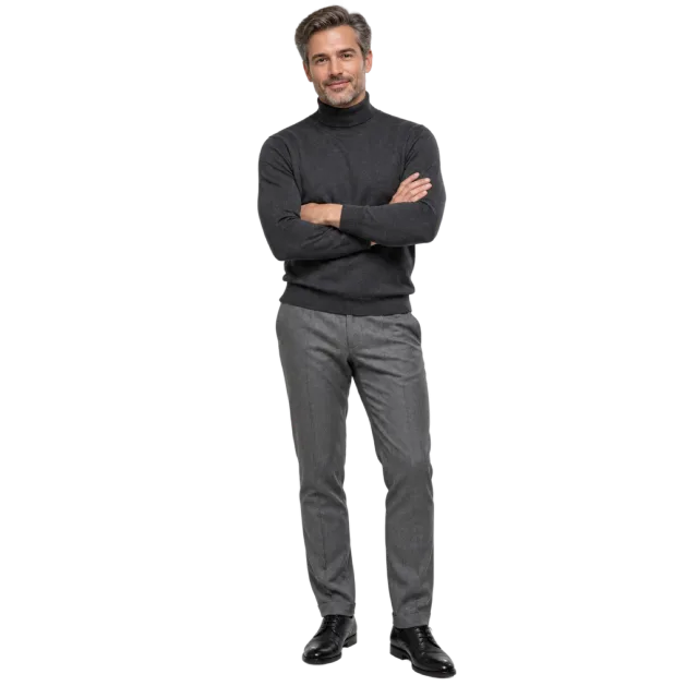 Man standing with folded arms in a charcoal turtleneck and grey trousers