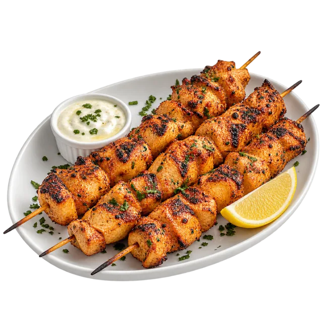 Shish tawook skewers with browned chicken pieces, a lemon wedge and white dipping sauce
