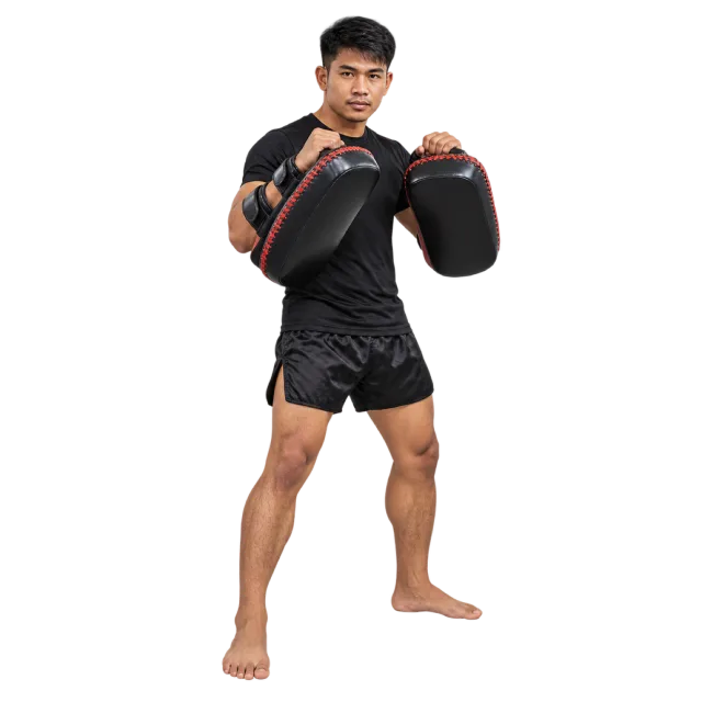 Coach in black sportswear holding black and red kick pads on the forearms