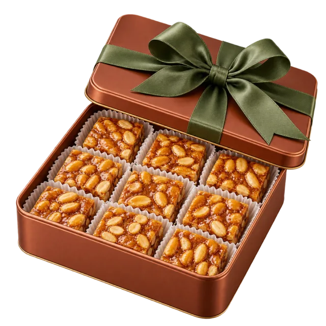 Copper-colored gift tin with peanut brittle squares and a green ribbon