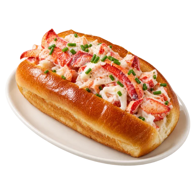 Split golden bread roll filled with lobster pieces and chopped green herbs on a white plate