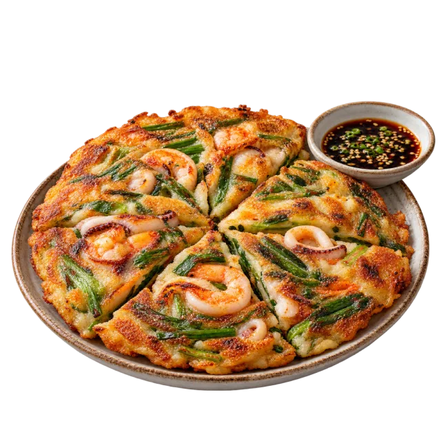 Sliced golden pancake with seafood and green onions beside a small dipping bowl