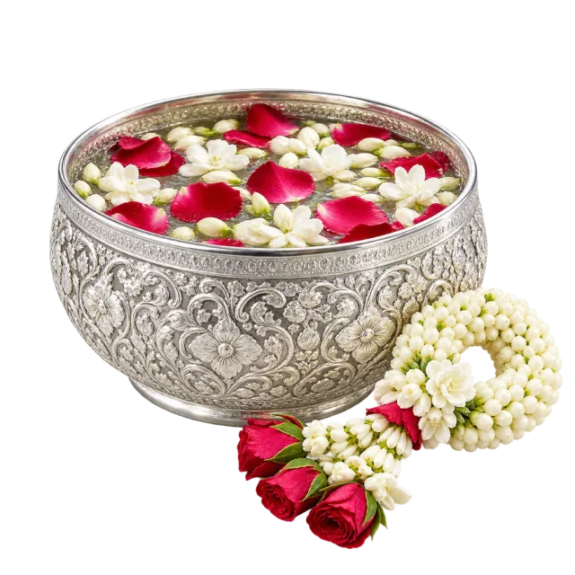 Ornate silver-colored bowl of water and flower petals beside a white and red garland