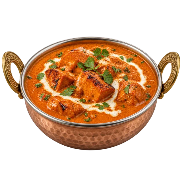 An orange chicken curry with cream swirls and herbs in a handled copper bowl
